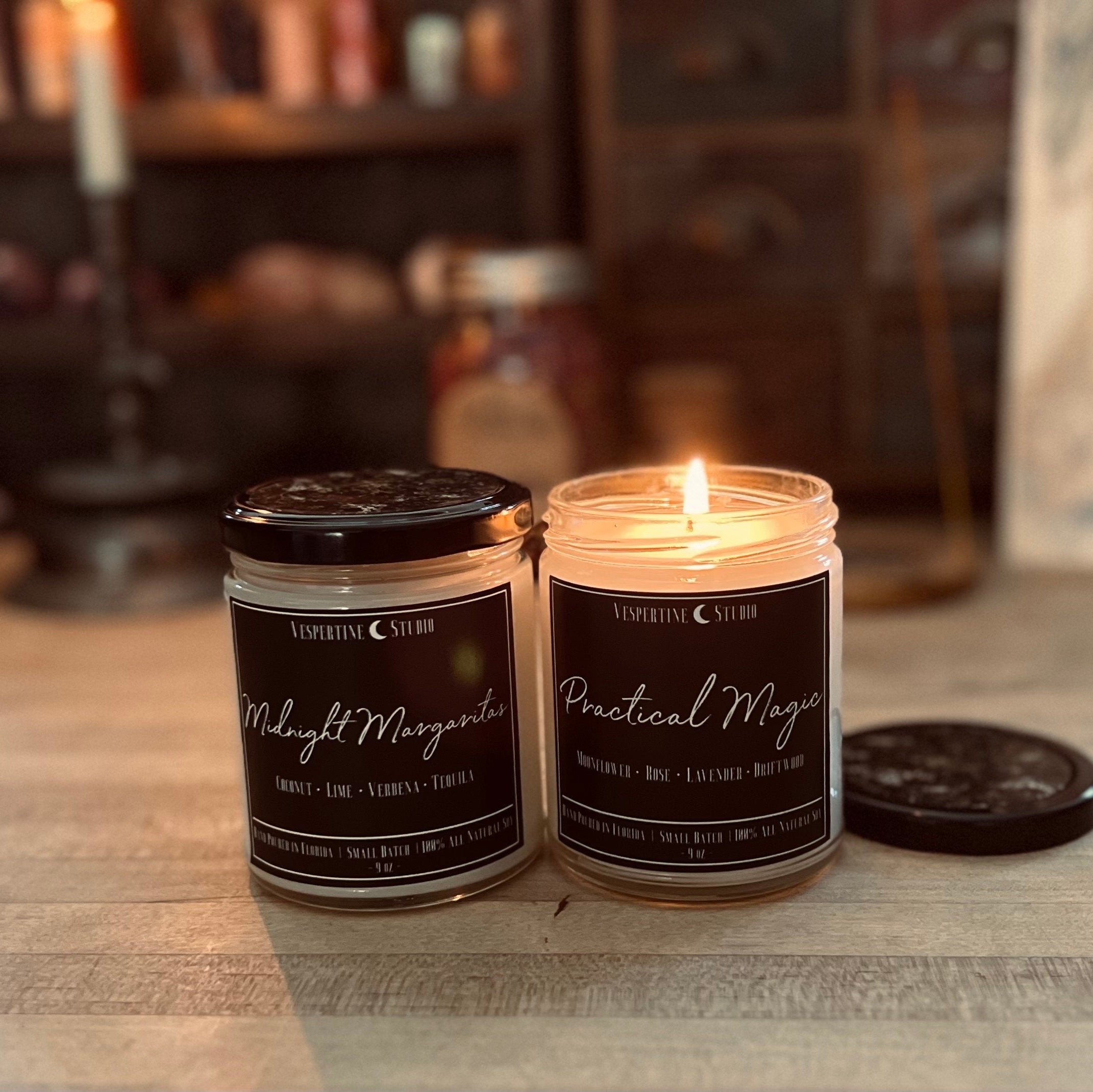 Two candles with black labels on a wooden surface, with a blurred background.